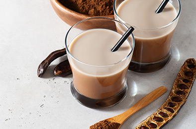 Carob drinks in glass with carob beans and powder